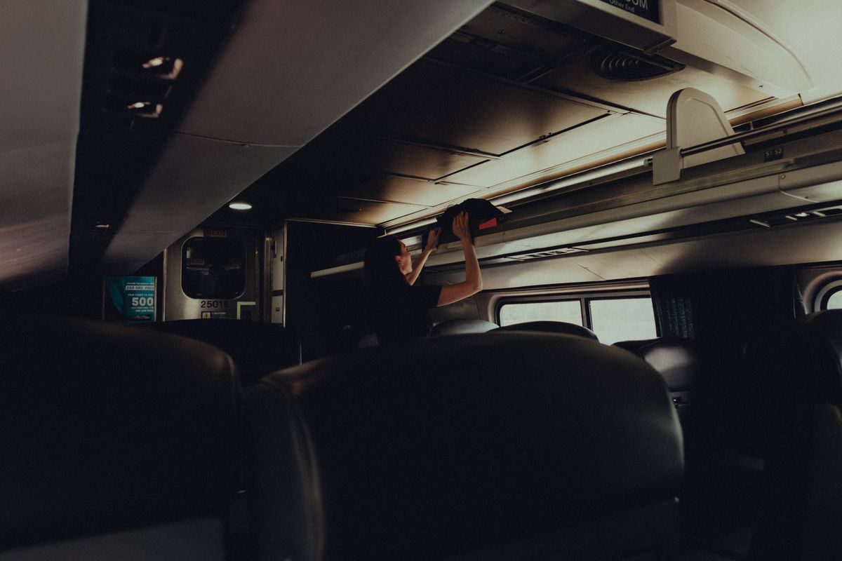 A woman placing her bag in the overhead rack on a modern train.