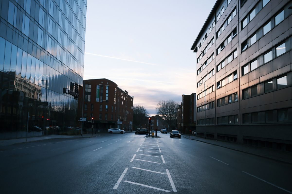 Empty city street at dusk, tall buildings reflecting soft evening light, creating a serene urban scene.