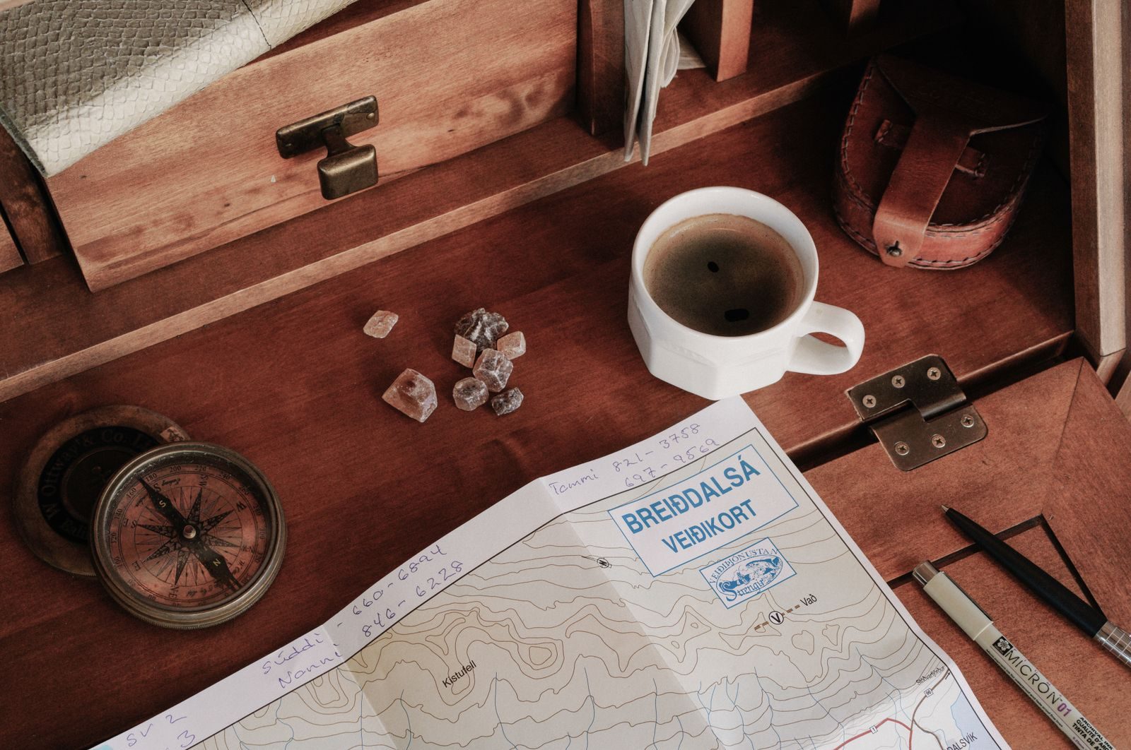 A top-down view of a rustic workspace featuring a map, compass, and a cup of coffee.