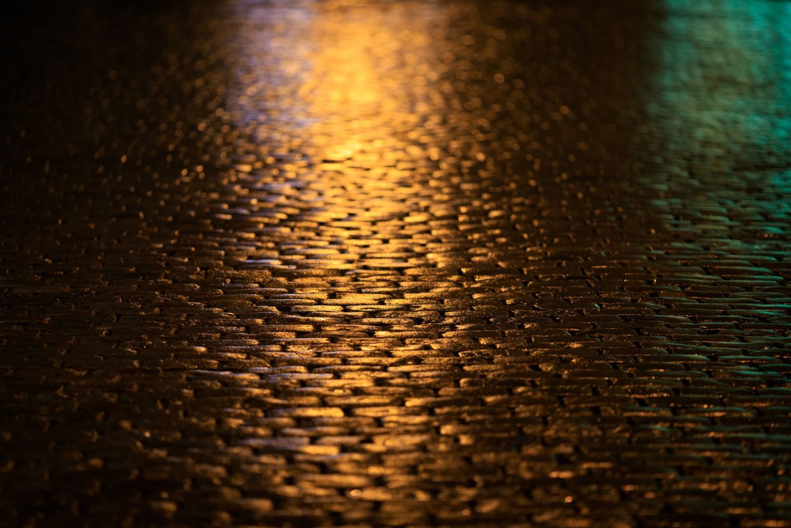 A moody night scene of a cobblestone street reflecting warm and cool lights.
