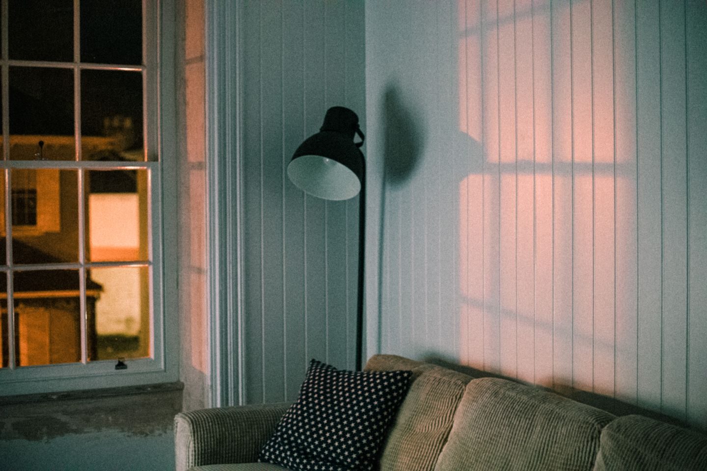 A warm living room with a soft couch and a floor lamp casting shadows on the wall
