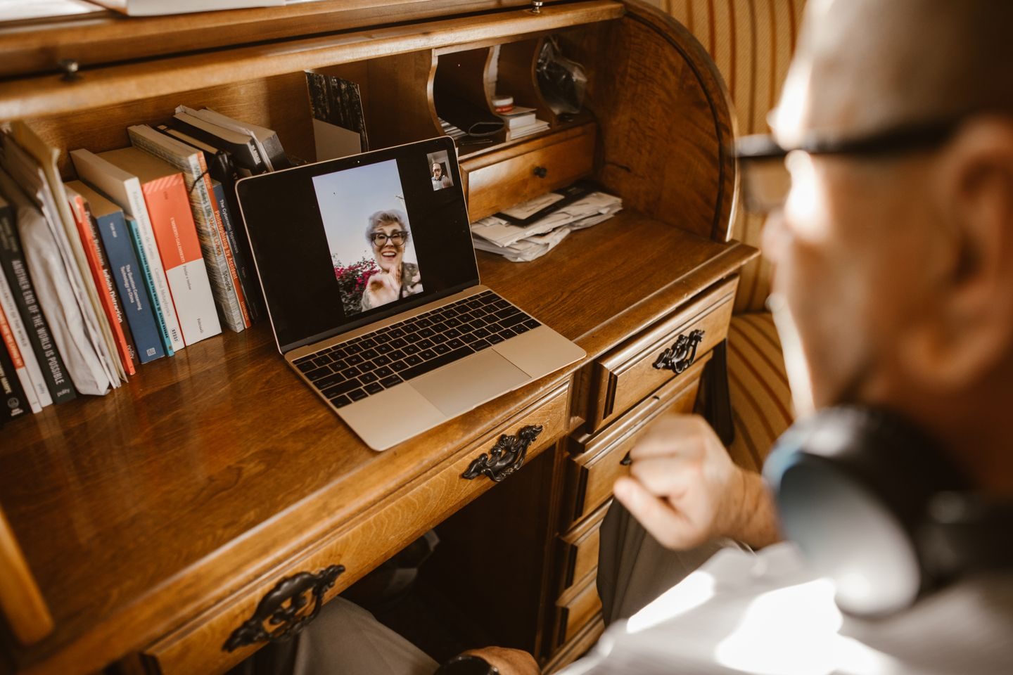 A man video calling from a laptop on a wooden desk