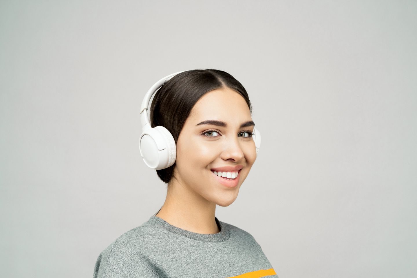 A woman wearing white wireless headphones, smiling while listening to music at home