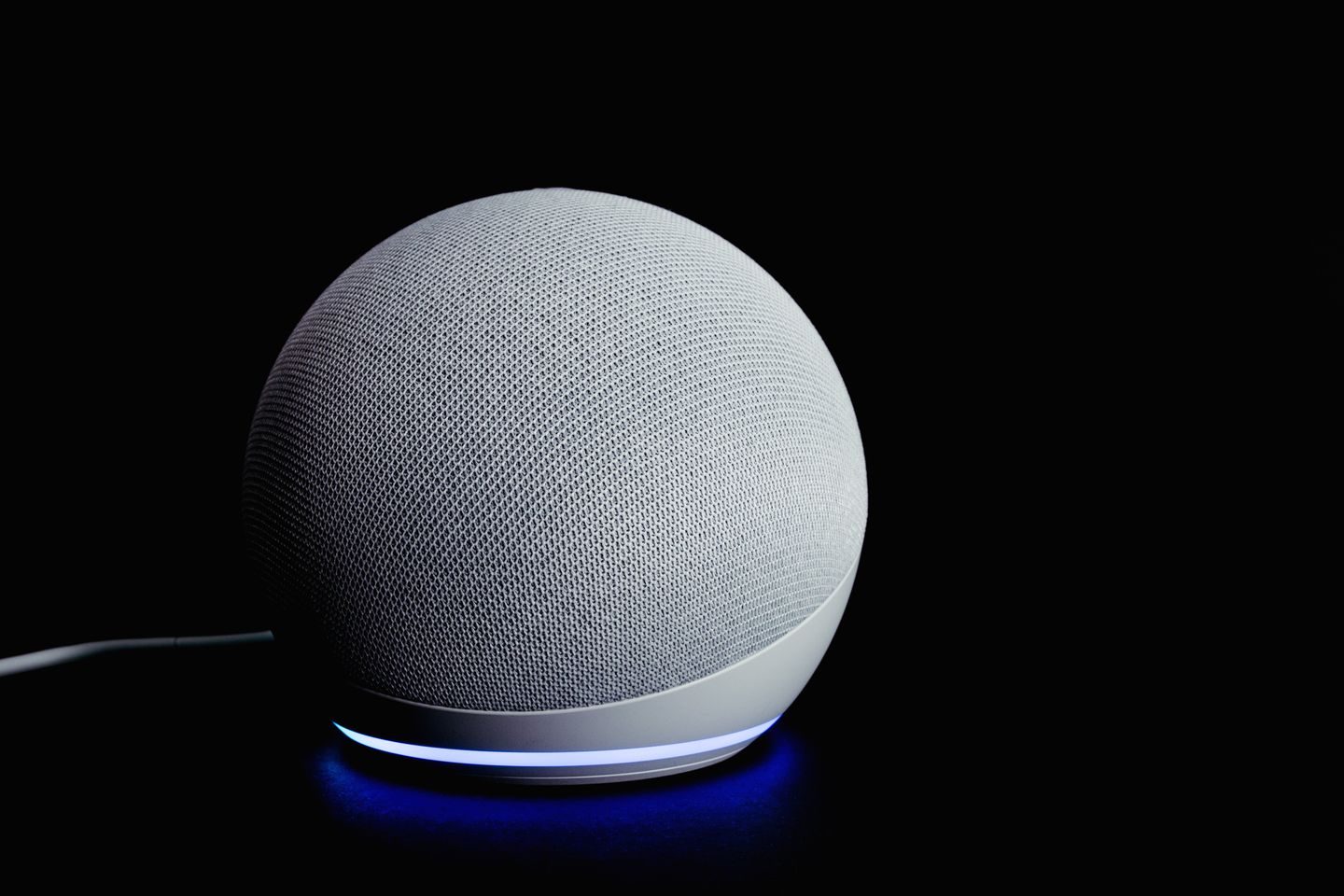 Photograph: Modern smart speaker device with illuminated ring, featured on a dark background.