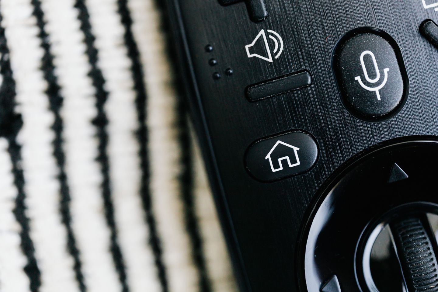 Photograph: Detailed macro shot of a sleek black remote control with microphone button and textured background.