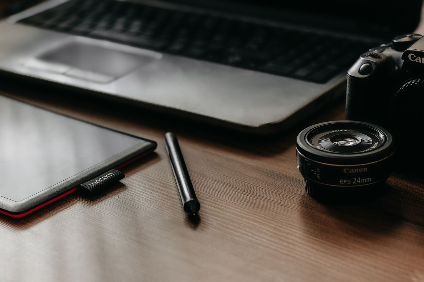 Photograph: A workspace featuring a laptop, tablet, camera, and lens, ideal for creative work and photography.